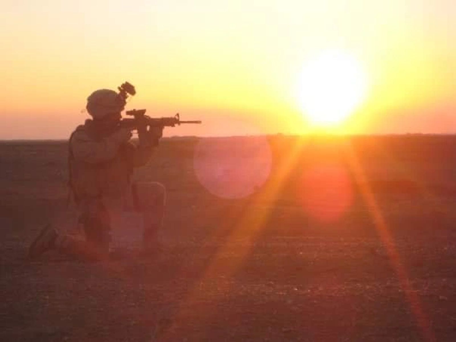 A soldier kneels in silhouette against a desert sunrise